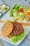 Delicious grilled  burger on white plate on wooden table.  with sauces, french fries and salads