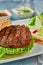 Delicious grilled  burger on white plate on wooden table.  with sauces, french fries and salads