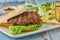 Delicious grilled  burger on white plate on wooden table.  with sauces, french fries and salads