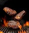 Delicious grilled pork or beef steaks are falling down on black background. Barbecue bbq grill, flaming fire, ember