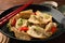 Delicious gyoza (asian dumplings) with sesame seeds, green onions and chili peppers on table