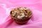 Delicious and healthy mixed dried fruit, nuts and seeds in a wooden bowl on pink silky background