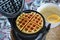 Delicious homemade Belgian waffle. Bright Sunday morning breakfast with tasty waffle. Batter and waffle maker in background