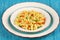 Delicious homemade fusilli pasta cooked with basil pesto, carrots, corn and peas in a plate on a turquoise blue napkin
