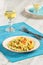 Delicious homemade fusilli pasta cooked with basil pesto, carrots, corn and peas in a plate on a turquoise blue napkin, served