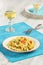 Delicious homemade fusilli pasta cooked with basil pesto, carrots, corn and peas in a plate on a turquoise blue napkin, served wit