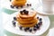 Delicious homemade pancake tower with maple sirup and organic blueberries on the white plate next the cup of coffee. Sweet breakfa