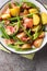 Delicious homemade potato salad with bacon and green beans close-up in a bowl on the table. Vertical top view