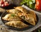 Delicious Indian samosa pastry presented on a plate with tomatoes and lettuce on a wooden table.