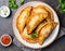 Delicious Indian samosa pastry presented on a plate with tomatoes and lettuce on a wooden table.