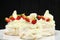 Delicious light meringue cakes with cream decorated with fresh halves of strawberries on a black background. Tasty
