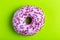 Delicious lilac donut with sprinkle on bright green background