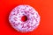 Delicious lilac donut with sprinkle on bright red background