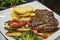 Delicious meal with steak strips, potato chips and grilled veggies on a white plate, tasty dish including several food groups