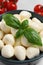 Delicious mozzarella balls and basil leaves in bowl, closeup