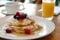 Delicious pancakes with syrup and summer berries on plate, orange juice in glass on wooden table