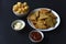 Delicious peppery nachos on a plate with sauces on a black background. Delicious snack with corn nachos close-up. Fast food