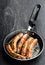 Delicious pork chipolatas sausages in a frying pan on black stone background