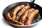 Delicious pork chipolatas sausages in a frying pan isolated on white