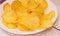 Delicious potato chips round shape, on a white plate on the background of a light wooden table, top view