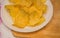 Delicious potato chips round shape, on a white plate on the background of a light wooden table, top view