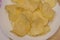 Delicious potato chips round shape, on a white plate on the background of a light wooden table, top view