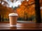 Delicious pumpkin spice latte cappuccino in a to go paper cup standing on a bench in autumn park