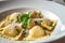 Delicious Ravioli dish served in a white plate with steam rising above, garnished with fresh basil leaves