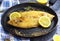 Delicious ready sole fish on black pan and decorated with lemon and herbs