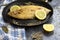 Delicious ready sole fish on black pan and decorated with lemon and herbs