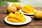 Delicious ripe cut and whole mangos on wooden table