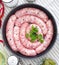 Delicious rustic raw meat sausages in frying pan, with bay leaves and fresh herbs in the kitchen.