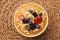 Delicious smoothie bowl with fresh berries, banana and oatmeal on woven mat, top view