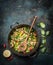 Delicious steamed healthy vegetables in cooking pan with ingredients and wooden spoon on dark rustic background, top view.