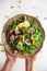 Delicious summer salad with edible flowers, vegetables, fruit, microgreens and cheese. Woman holding plate with salad, top view.