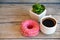 Delicious sweet fresh pink donut and cup of coffee on wooden background. Breakfast, fast food, bakery concept.