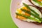 Delicious toast bread sandwiches with asparagus and fried eggs on pink plate over green background