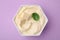 Delicious tofu sauce and basil leaf in bowl on violet background, top view