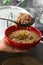 Delicious typical Central American dish called pozole served by an adult cook with a metal ladle in a red bowl and a pot almost