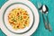 Delicious, vegetarian fusilli pasta with basil pesto, carrots, sweet corn and green pea in a plate on a turquoise tablecloth