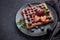 Delicious waffles with berries, mint and sweet sauce on black plate on grey background. Top view. Sweet meal. Dessert