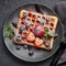Delicious waffles with berries, mint and sweet sauce on black plate on grey background. Top view. Sweet meal. Dessert