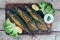 A deliciously roasted mackerel on a grill, presented on a wooden board, and along the leaves of green salad and pieces of lemon