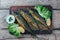 A deliciously roasted mackerel on a grill, presented on a wooden board, and along the leaves of green salad and pieces of lemon
