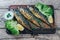 A deliciously roasted mackerel on a grill, presented on a wooden board, and along the leaves of green salad and pieces of lemon