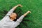 Delighted afro-american teenager is enjoying music while laying on the grass and raising hands.