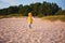 Delighted baby boy having fun, running on the sandy autumn beach near the pine tree forest