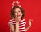 Delighted funny woman in a Christmas reindeer costume laughs and blows a kiss on colorful red background