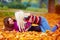 Delighted girls, friends having fun among fallen leaves in autumn park