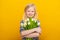 Delighted little girl with toothy smile, blonde hair, holds nice bouquet of white tulip flowers, isolated against yellow